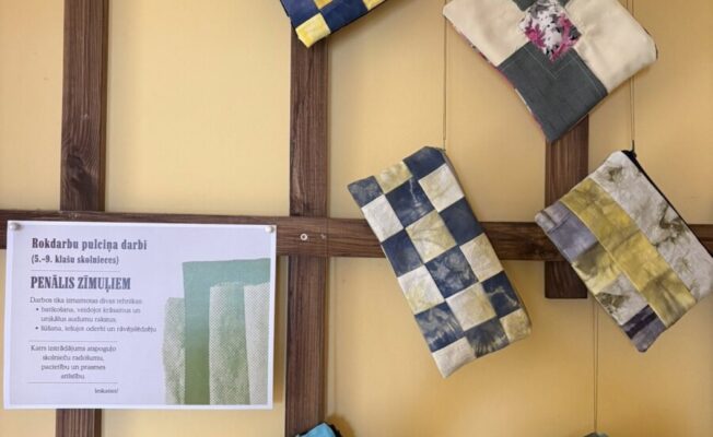 Uz dzeltenas sienas ar koka rāmjiem izvietoti seši ar rokām darināti, stepēti penāļi. Blakus tiem atrodas balta zīme ar tekstu 