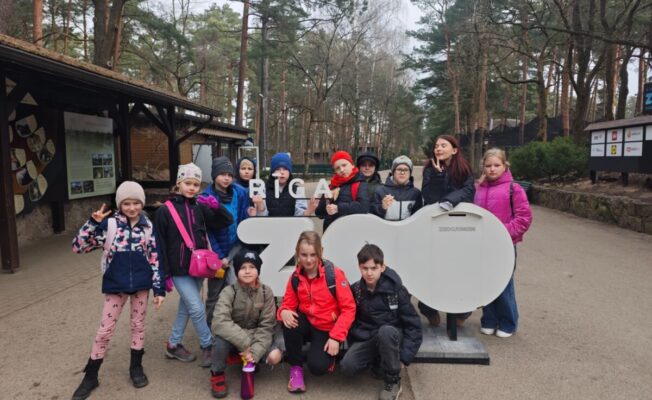 3.klases skolēni pozē pie liela balta uzraksta 