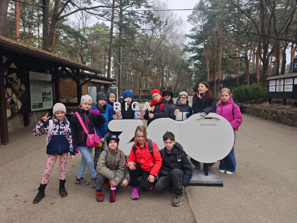 3.klases skolēni pozē pie liela balta uzraksta 