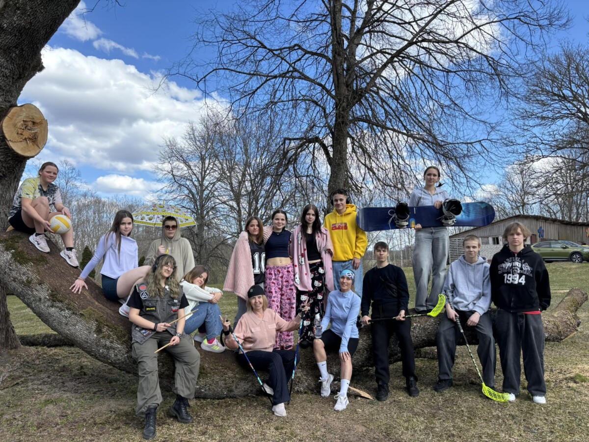 Grupa jauniešu (Birzgales pamatskolas 8.un 9.klašu skolēni) un klašu audzinātājas Baiba Liepiņlauska un Valija Skuja brīvā dabā, daži sēž uz liela nokritušā koka stumbra. Viņi tur dažādu sporta inventāru: volejbola bumbu, snovborda dēli, florbola nūjas un bungu vālītes. Vienam jaunietim mugurā ir džemperis ar uzrakstu 